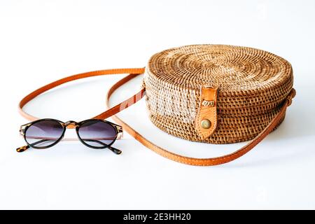 Sac rond ATA en rotin style boho avec bandoulière en cuir et lunettes de soleil, isolé sur fond blanc Banque D'Images