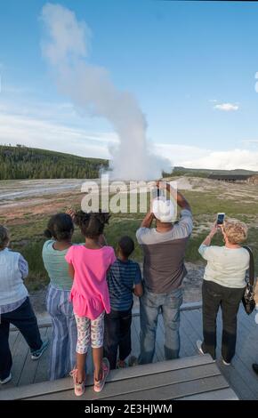 Les visteurs regardent l'éruption du geyser Old Faithful dans le parc national de Yellowstone, Wyoming, États-Unis. Banque D'Images
