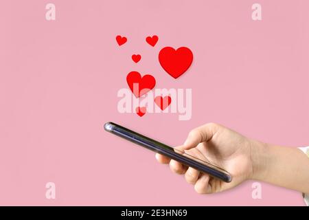 Mains de femmes tenant un téléphone portable avec des coeurs, symbole Amour sur fond rose. Concept de la Saint-Valentin. Banque D'Images