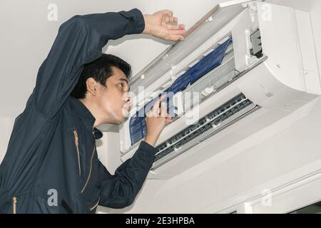 Les réparateurs de climatisation en uniforme bleu vérifient et réparent l'air suspendu au mur. Banque D'Images