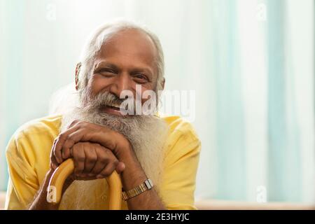 UN VIEIL HOMME HEUREUX REGARDANT L'APPAREIL PHOTO TOUT EN ÉTANT ASSIS AVEC UN BÂTON DE MARCHE Banque D'Images