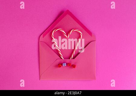 Fond rose festif. Cœurs de bonbons dans l'enveloppe. Perles de cube en bois colorées avec le mot « Love ». Saint Valentin. 14 février. Pose à plat, Banque D'Images