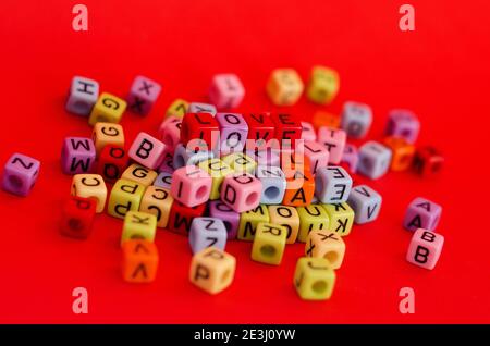 Perles de cube en bois colorées avec lettres sur fond rouge festif, mot « Love ». Saint Valentin. 14 février. Flat lay, vue de dessus. Banque D'Images