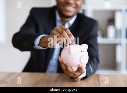 Récolte d'homme d'affaires noir mettant de l'argent dans une banque de pigey Banque D'Images