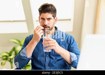 Photo d'un homme d'affaires avec une pilule dans sa main, stressant lorsqu'il est assis derrière son ordinateur portable et souffrant d'une forte douleur à la tête. Banque D'Images