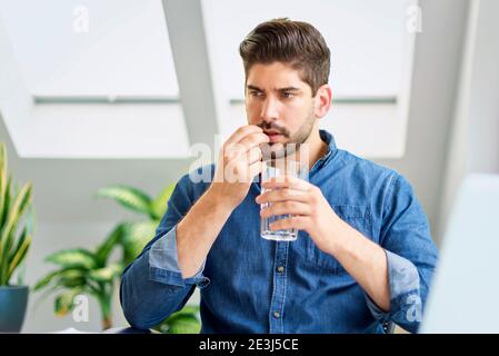 Photo d'un homme d'affaires avec une pilule dans sa main, stressant lorsqu'il est assis derrière son ordinateur portable et souffrant d'une forte douleur à la tête. Banque D'Images
