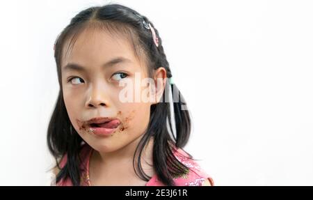 Gros plan visage asiatique mignon enfant fille avec désordre de chocolat autour de sa bouche, regarder à l'espace vide sur le côté pour la copie, les produits ou le design, la langue Banque D'Images