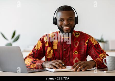 E-learning. Un homme noir heureux portant un casque étudier en ligne avec un ordinateur portable à la maison Banque D'Images