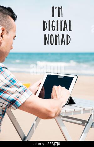 Le texte Je suis un nomade numérique et un jeune homme caucasien sur la plage, en utilisant une tablette numérique, assis à une table extérieure, avec l'océan à l'arrière Banque D'Images