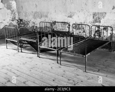 Quatre vieux lits rouillés dans une chambre abandonnée. Image en noir et blanc Banque D'Images