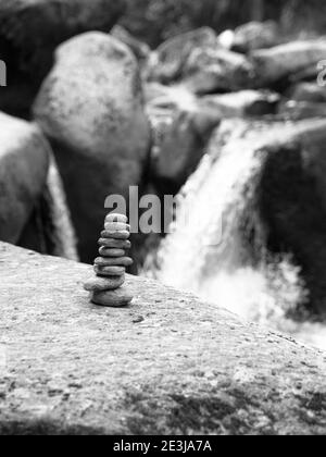 Pyramide de galets équilibrée avec cascade de rivière non concentrée sur fond . Image en noir et blanc. Banque D'Images