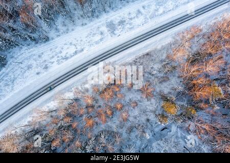 Vue aérienne depuis un drone de voiture sur une neige sinueuse couverte route dans la forêt d'hiver Banque D'Images