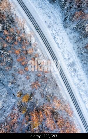 Vue aérienne depuis un drone de voiture sur une neige sinueuse couverte route dans la forêt d'hiver Banque D'Images