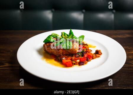 Morceau de viande juteux avec des légumes en sauce au basilic et à la crème sur une assiette blanche. Banque D'Images
