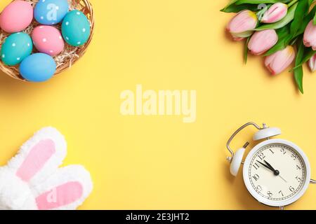 Joyeuses Pâques. Œufs multicolores, tulipes et réveil sur fond jaune. Carte de vœux d'invitation à poser à plat avec espace de copie. Banque D'Images