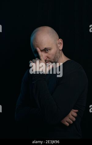 Un homme chauve attentionné tient sa main à la tête. Problèmes et crise des hommes d'âge moyen. Portrait dans un style sombre. Banque D'Images