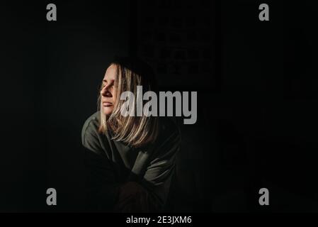 Femme blonde avec arrière-plan sombre, dans la lumière avec les yeux se ferment Banque D'Images