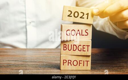 Homme d'affaires met des blocs de bois avec les mots 2021, objectifs, budget, profit. Planification, plans et tâches. De nouvelles idées commerciales. Définition de l'objectif, de la cible. Motiva Banque D'Images