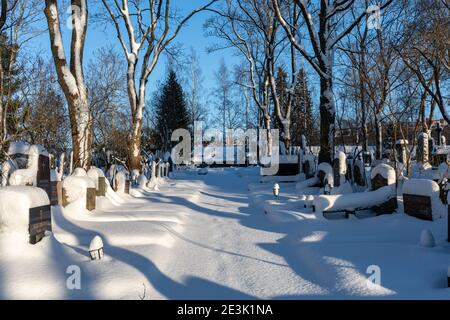 Des tombes et des pierres à tête recouvertes de neige au cimetière Hietaniemi, lors d'une journée d'hiver ensoleillée à Helsinki, en Finlande Banque D'Images