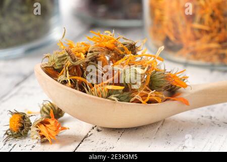 Cuillère en bois de fleurs de calendula saines séchées. Pots en verre de pétales de marigold séchés et d'herbes médicinales sur fond. Médecine alternative. Banque D'Images