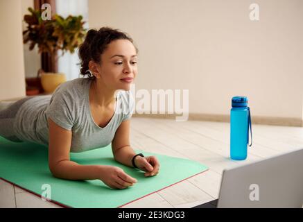Gros plan d'une femme faisant de l'exercice de planche tout en regardant des tutoriels de fitness sur ordinateur portable. Fitness en ligne pendant le confinement en cas de pandémie Banque D'Images