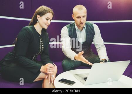Deux partenaires commerciaux disposent d'une visioconférence sur ordinateur portable un canapé violet dans un espace de bureau moderne avec un accent sélectif sur une femme entre Banque D'Images