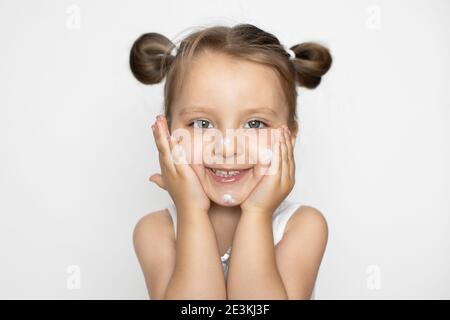 Caucasien mignon bébé portant le dessus blanc après avoir pris une douche, l'application de crème hydratante ou de lotion pour bébé sur son visage. Hygiène et soins de la peau pour bébé Banque D'Images