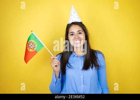 Jeune femme caucasienne portant un chapeau d'anniversaire sur un jaune isolé Arrière-plan souriant et portant un drapeau portugais Banque D'Images