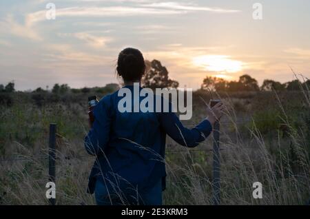 une fille regardant le coucher du soleil et buvant son compagnon dans la campagne Banque D'Images