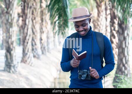 Homme de voyage africain tenant l'appareil photo et regardant passeport avec le sourire et heureux Banque D'Images