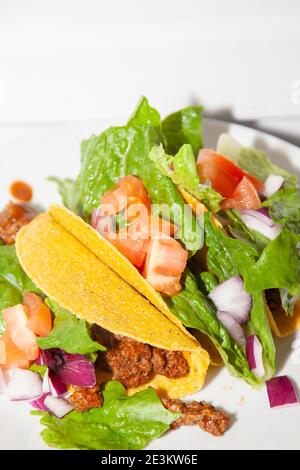 Trois tacos de bœuf haché et de salade faits avec de la laitue romaine, des tomates en dés et des oignons violets en dés sur une assiette blanche Banque D'Images