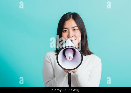 Belle femme asiatique sourit elle tenant le mégaphone faire l'annonce, femme excitée gaie annoncer de bonnes nouvelles isolées sur un fond bleu Banque D'Images