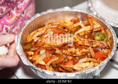 Femme ouvrant un moule à emporter de poulet sauté dans un moule de service avec des jalapenos, des poivrons verts rôtis, des oignons rôtis et du poivron rouge rôti Banque D'Images