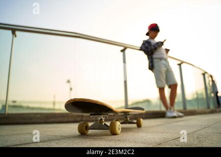 adolescent asiatique skateboarder garçon regardant le téléphone mobile tout en se reposant, se concentrer sur le skateboard Banque D'Images