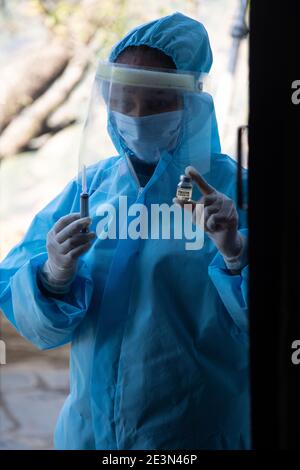 Jeune femme médecin en uniforme médical tenant une seringue et un vaccin contre le virus corona, debout devant la porte du village. Banque D'Images