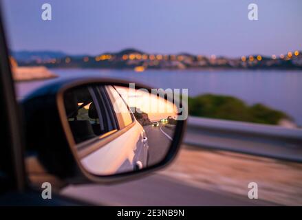 Voyager en voiture le long de la magnifique côte la nuit. Reflet du coucher de soleil sur le miroir latéral. Banque D'Images