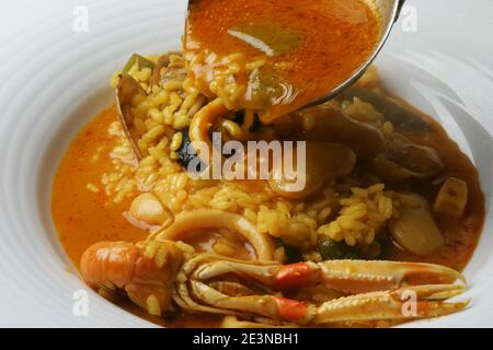 Action de servir un bouillon de riz, avec des fruits de mer et des légumes Banque D'Images