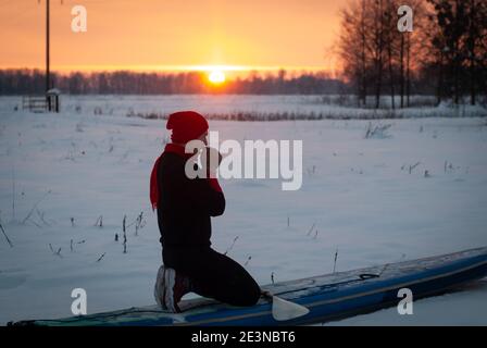 un homme sportif dans un chapeau rouge avec une paddle se tient sur un panneau gonflable au milieu de la neige, le panneau de soutien d'hiver Banque D'Images