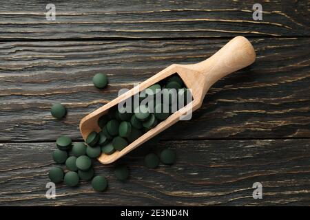Pelle en bois avec pilules de spiruline sur fond en bois, vue de dessus Banque D'Images