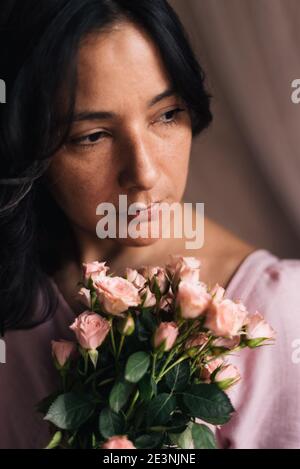 jeune femme thirtysomething portrait avec roses roses et lumière naturelle verticale gros plan. concept de milieu de vie femme sophistiquée. confiance féminité Banque D'Images