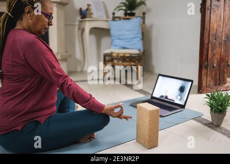 Femme africaine senior faisant la leçon de yoga en ligne à la maison pendant Isolation de verrouillage - concentrez-vous sur la main Banque D'Images