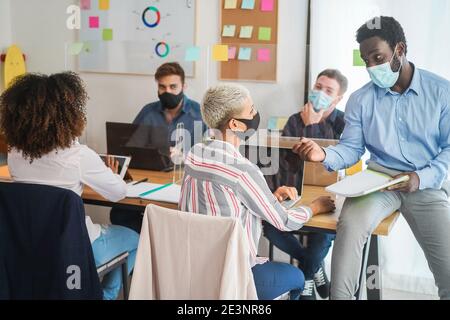 Jeunes multiraciaux avec des masques faciaux dans un bureau de coworking moderne portant des masques de protection pour la prévention de la propagation du coronavirus - Startup Banque D'Images