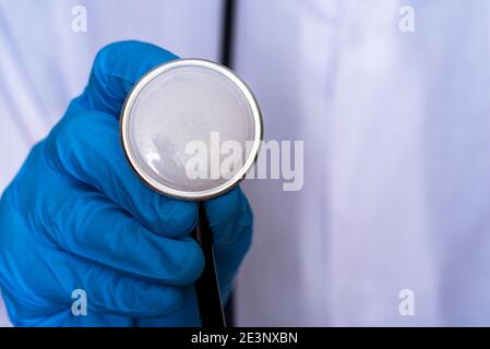 Une main dans un gant médical tire un masque médical sous un stéthoscope, le concept d'avoir à porter un masque médical. Banque D'Images