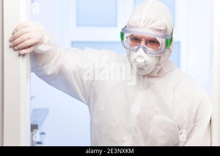 Médecin fatigué en raison de Covid-19 debout dans des vêtements de protection blancs et masque médical devant une chirurgie dans un hôpital - se concentrer sur le visage Banque D'Images