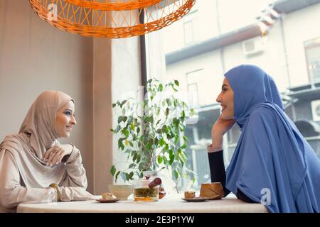 Parle. Belle réunion des femmes arabes au café ou au restaurant, entre amis ou réunion d'affaires. Passer du temps ensemble, parler, rire. Style de vie musulman. Modèles élégants et élégants avec maquillage. Banque D'Images