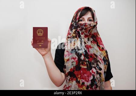 La jeune femme musulmane arabe vêtue de hijab tient le passeport de la République populaire de Chine sur fond de mur blanc, portrait de studio. Banque D'Images