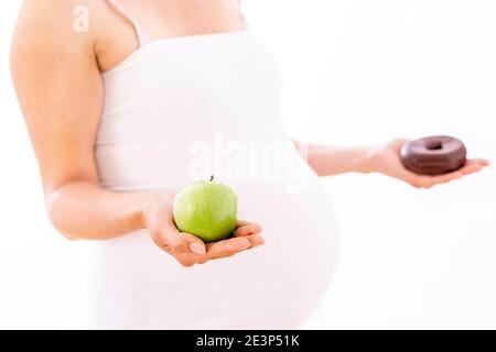 Femme enceinte choisissant une pomme saine plutôt qu'un beignet malsain sur blanc arrière-plan Banque D'Images