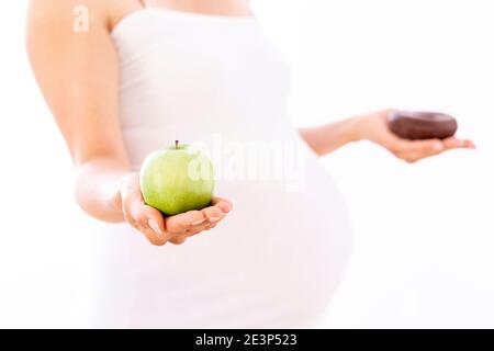 Femme enceinte choisissant une pomme saine plutôt qu'un beignet malsain sur blanc arrière-plan Banque D'Images