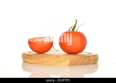 Une tomate juteuse biologique mûre rouge entière et une moitié de tomates vertes aux queues de cheval vertes, repose sur un support rond en bois, sur un fond blanc. Banque D'Images