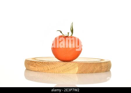 Une tomate juteuse biologique mûre rouge entière avec une queue de cheval verte, repose sur un support rond en bois, sur un fond blanc. Banque D'Images